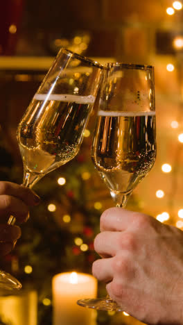 Vertical-Video-Of-Couple-Making-Christmas-Toast-With-Champagne-In-Front-Of-Fire-At-Home-With-Blue-Screen-Mobile-Phone